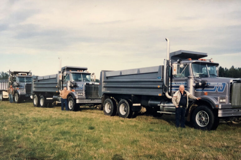 An older colour photo of three Michell team members posing next to their trucks, which are parked in single file.